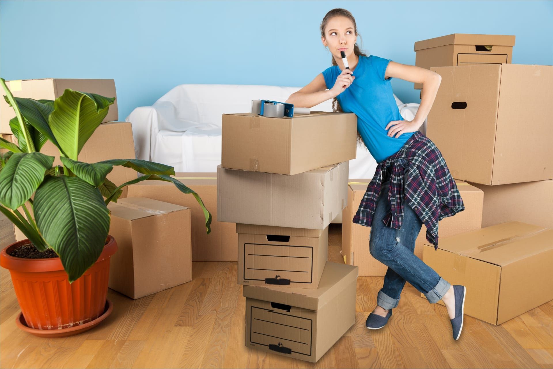Woman in a blue shirt leaning on a stack of moving boxes, thinking