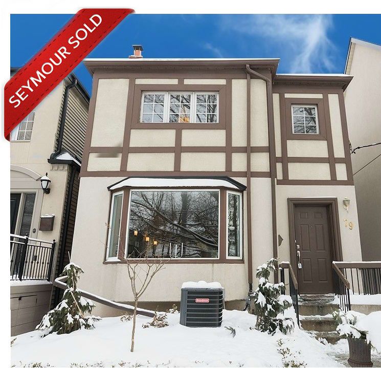 Two-storey stucco home with dark trim and a bay window in winter, with a Seymour Sold banner