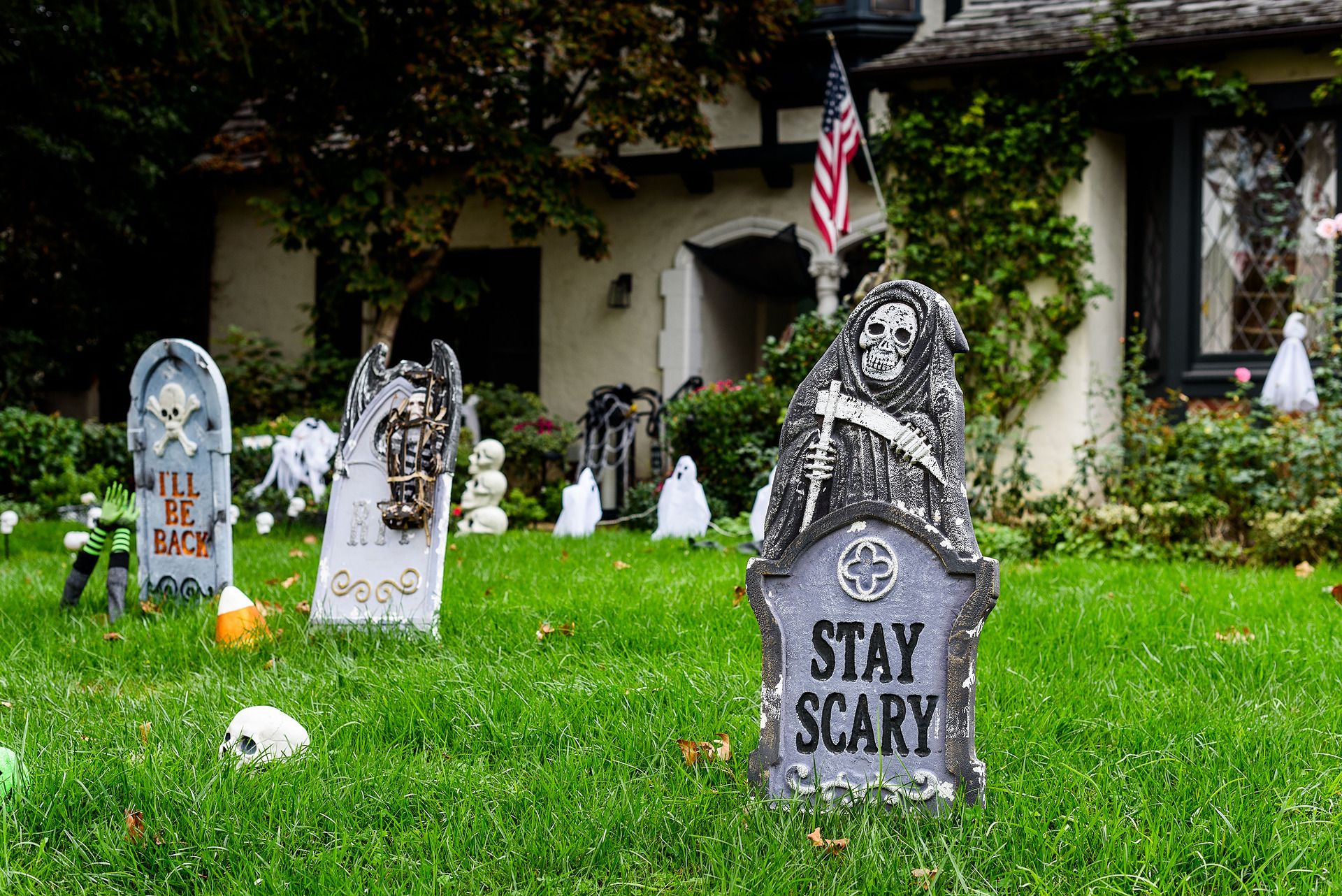 Halloween tombstones and skeleton decorations on a front lawn, one reading Stay Scary