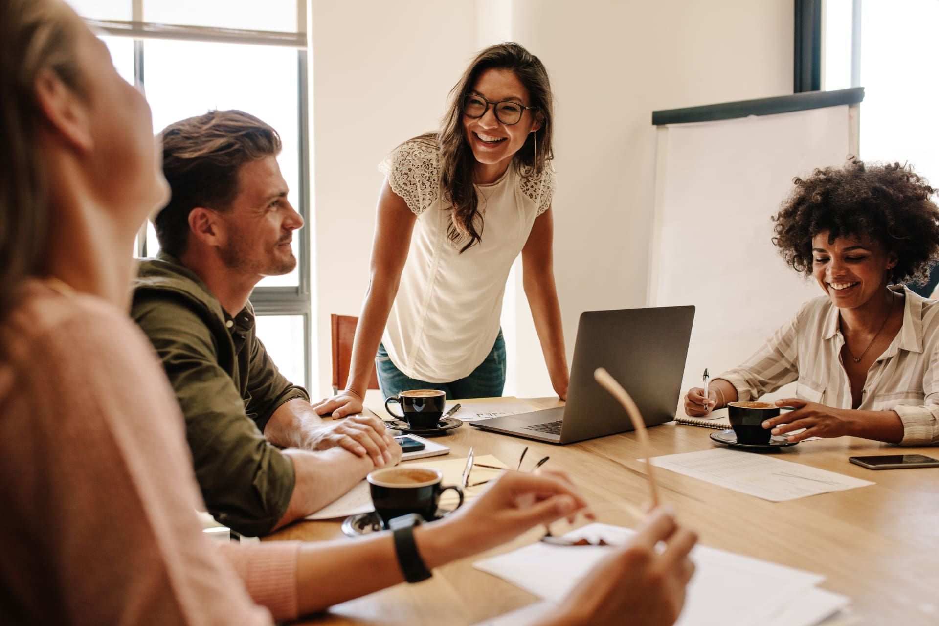 Group of colleagues smiling around a table with a laptop and coffee