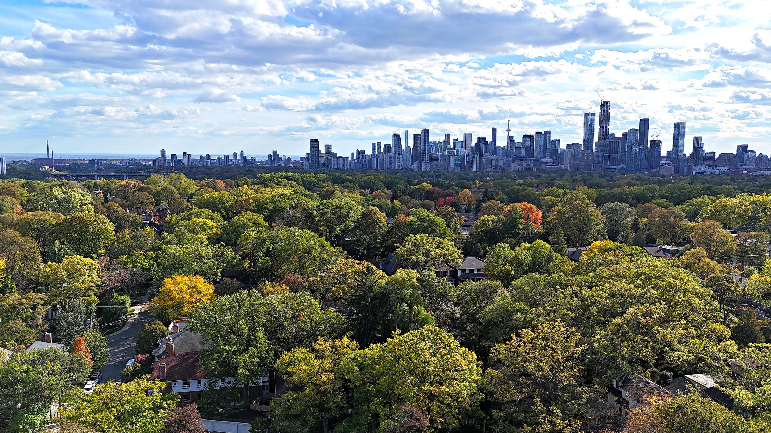 A drone view south over the fall trees of Moore Park to the downtown Toronto skyline and the CN Tower.