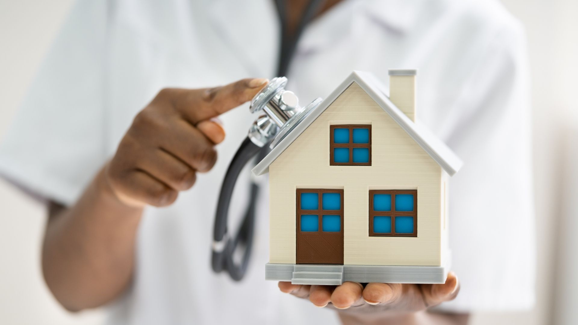 Doctor holding a model house and a stethoscope