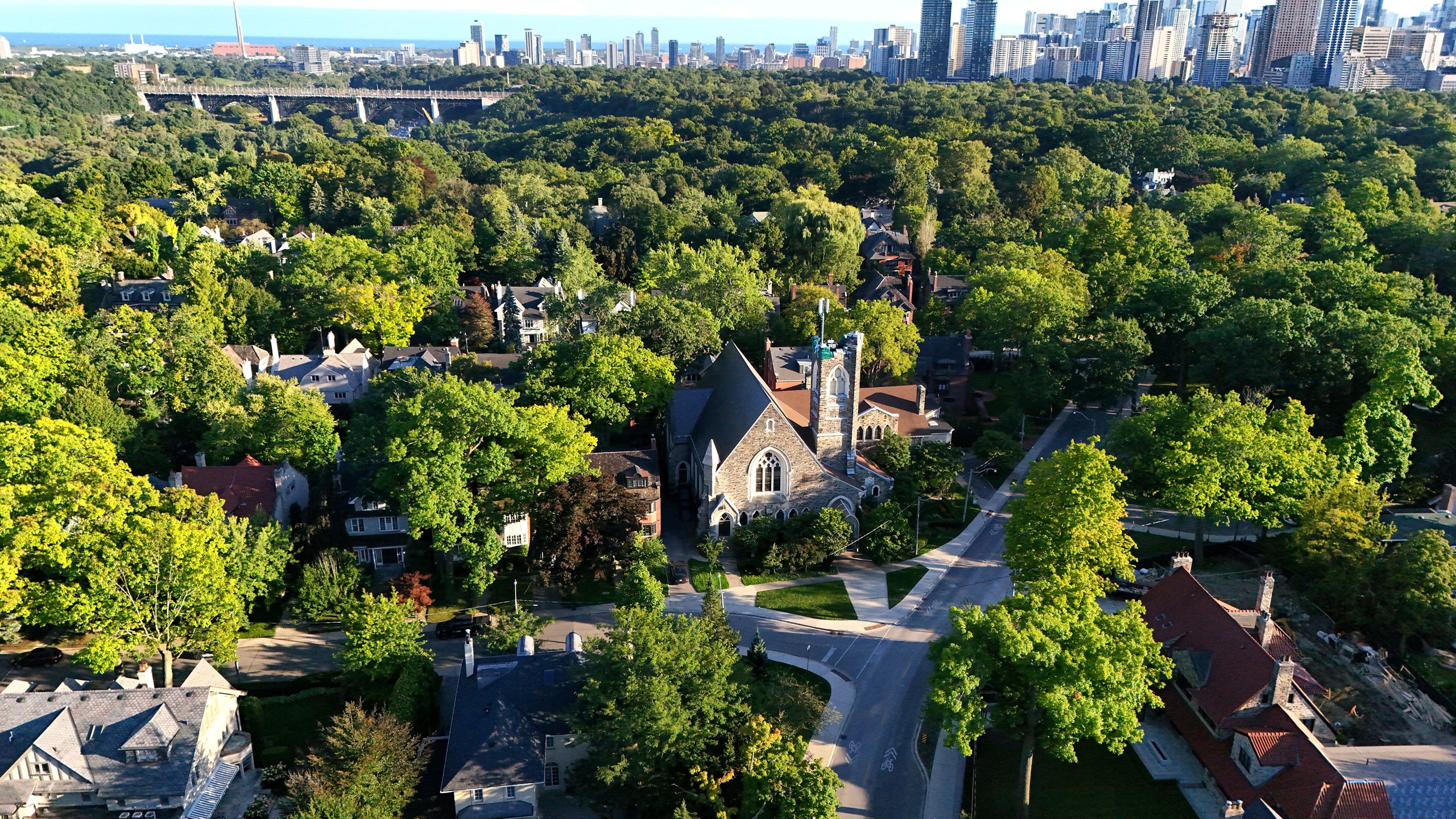 Drone view of Rosedale United Church and surrounding homes, with the Bloor Viaduct and the downtown skyline beyond, at golden hour.