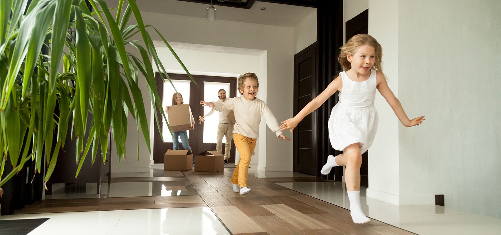 Children running into an empty home while their parents carry in moving boxes