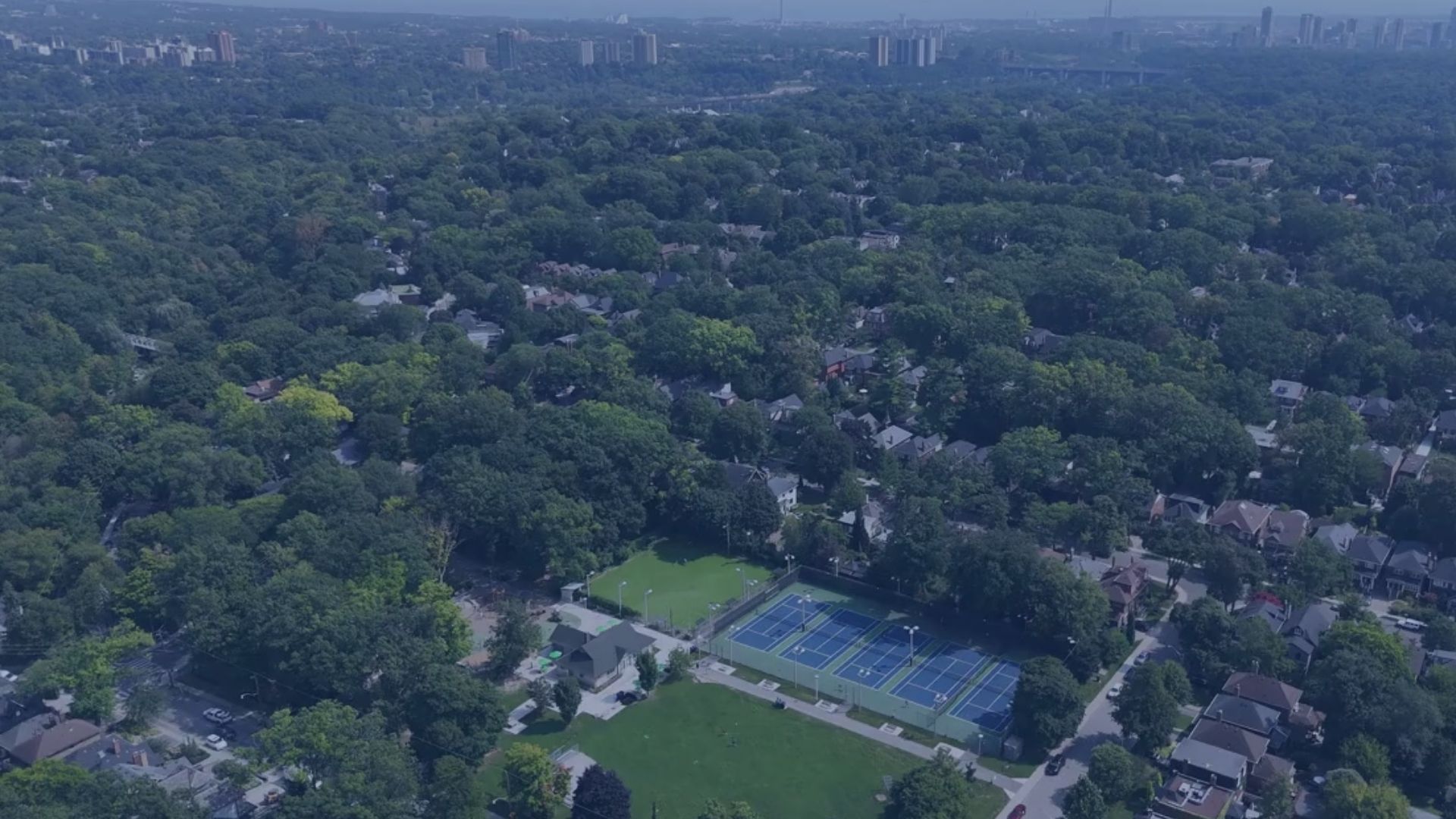 Aerial view of a wooded residential area with tennis courts and a park
